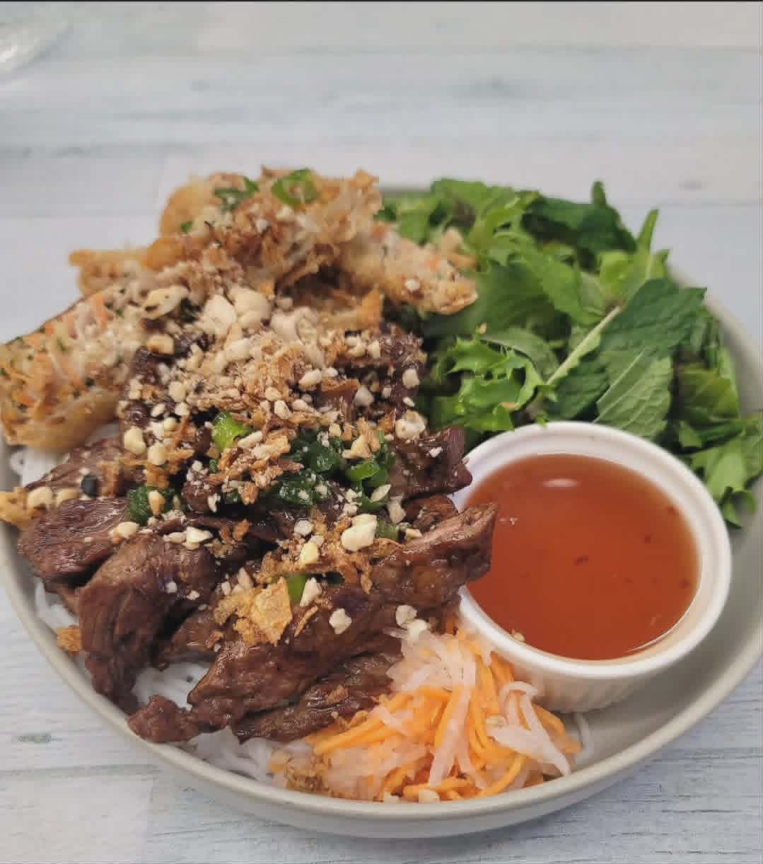Bún thịt nướng — grilled beef vermicelli bowl with a spring roll, fresh herbs and fish sauce.
